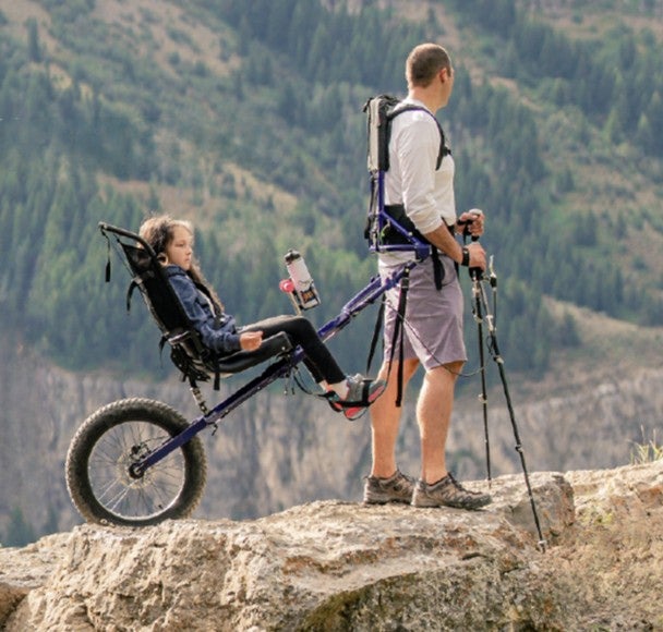 Picture of a man using a Huckleberry Hiker to carry a younger girl on a hike up a mountain.