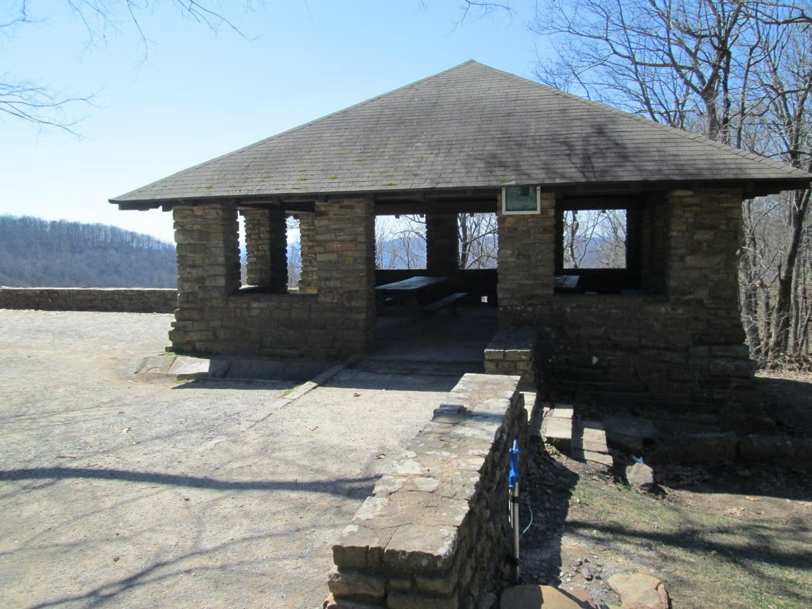 Stone pavilion overlooking small tree lined mountain range in the winter. No snow.
